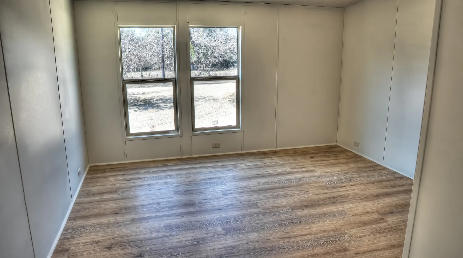 Room featuring wood-finish flooring, white baseboards, and two windows