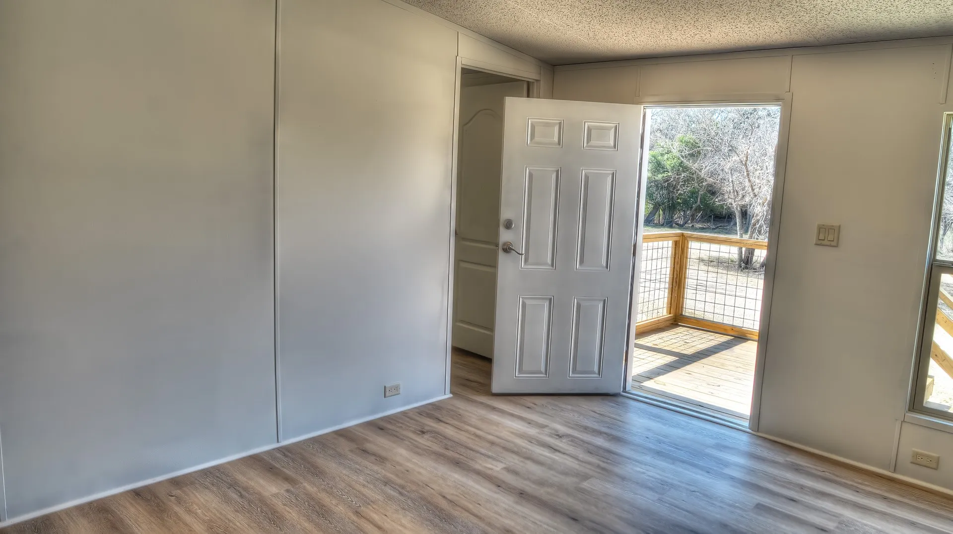 Interior room featuring wood-finish flooring, white panel walls, and a white paneled door opening to an outdoor deck