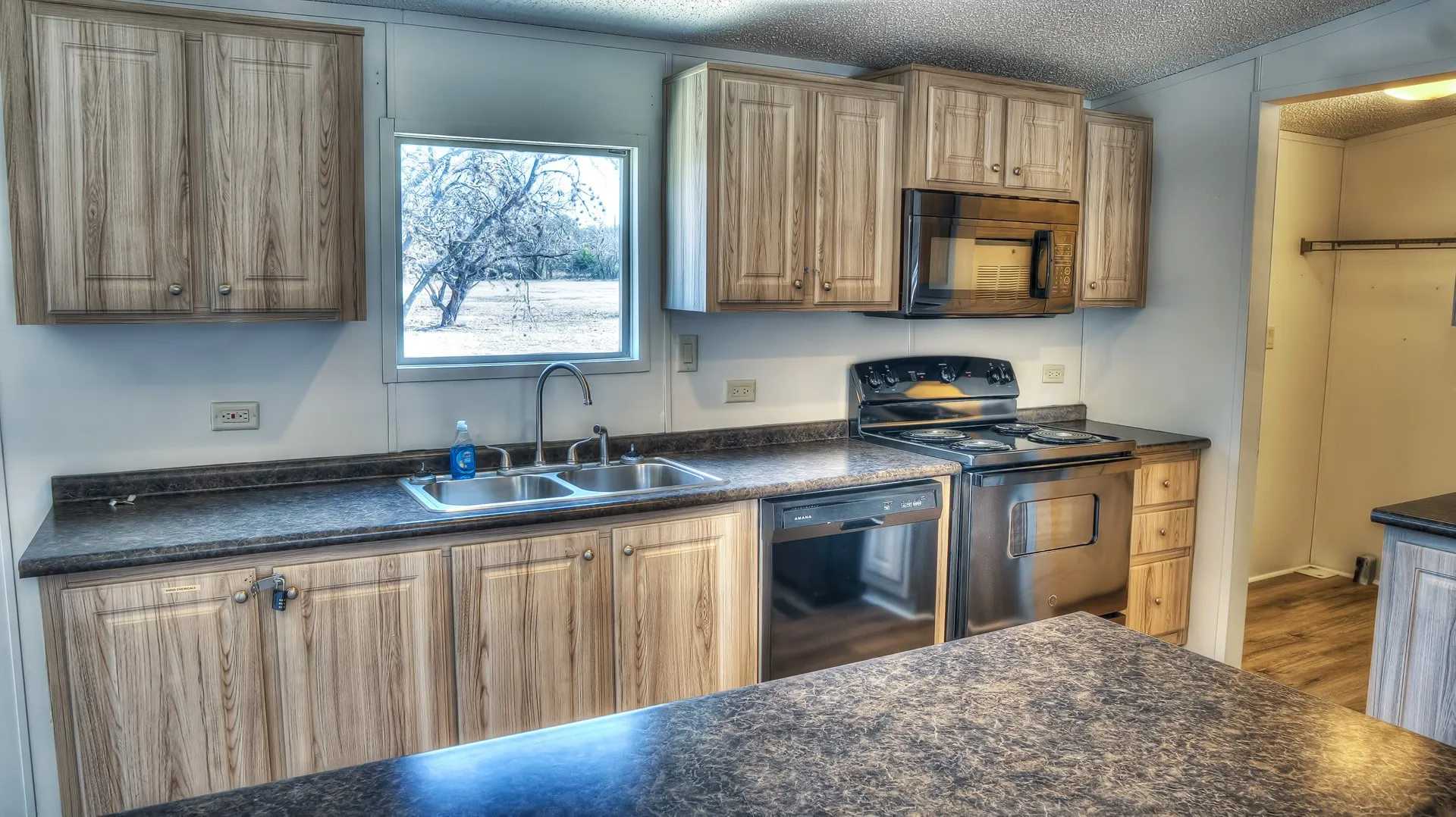 Kitchen featuring wood-finish cabinetry, dark speckled countertops, and a stainless steel double-basin sink