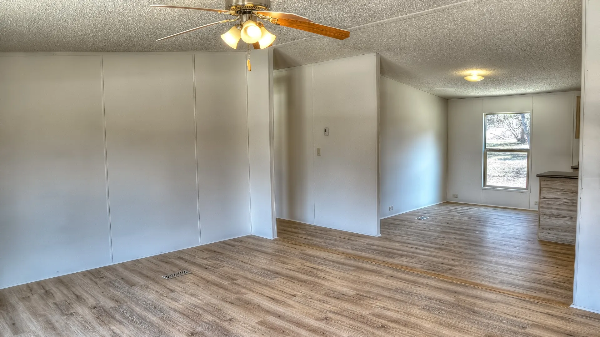 Spacious living area featuring wood-finish flooring, white paneled walls, and a ceiling fan with integrated lighting