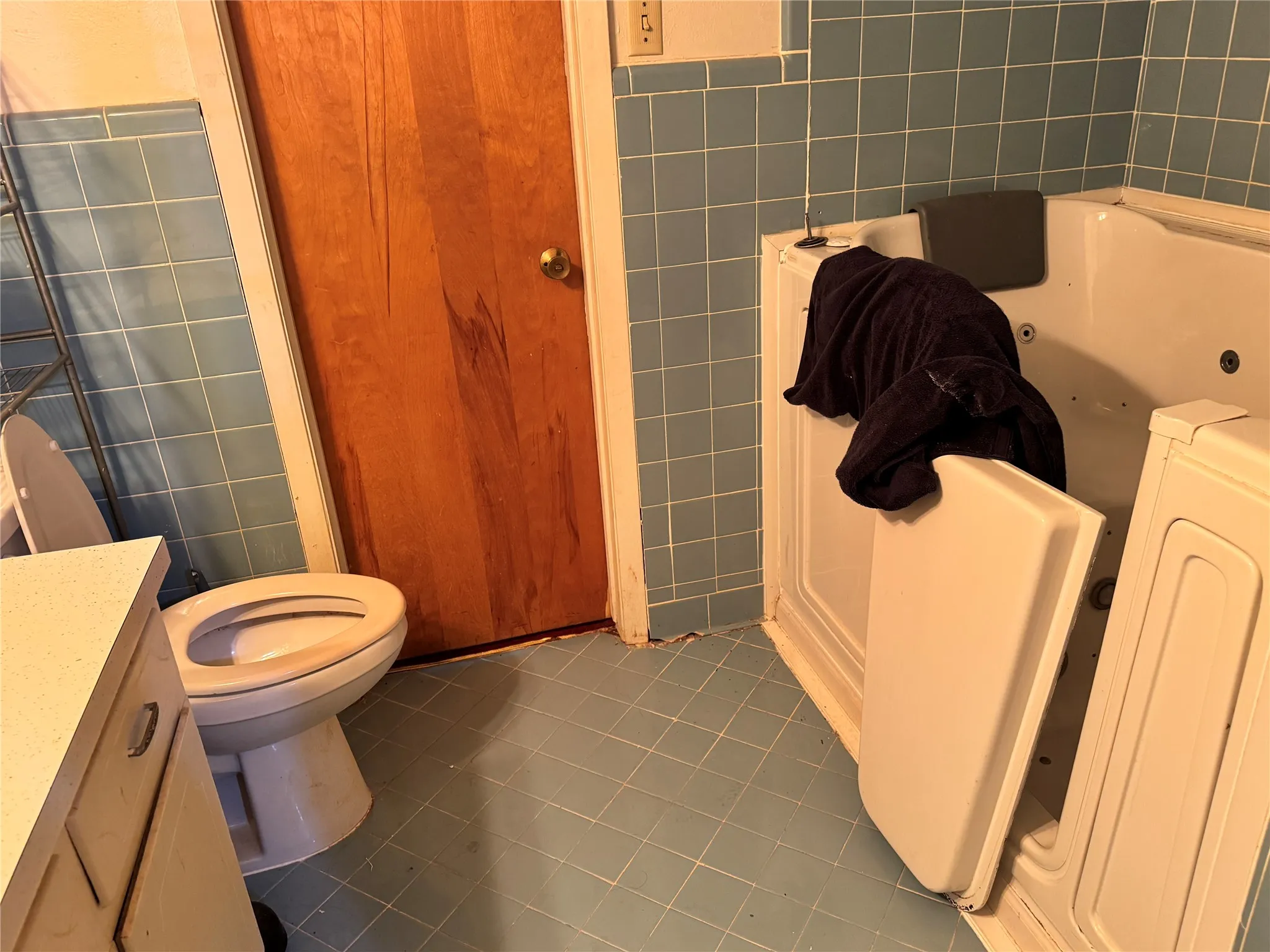 Bathroom featuring a walk-in tub, blue square tile flooring, blue square wall tiles, a wood-finish interior door, and a white vanity with a light-colored countertop