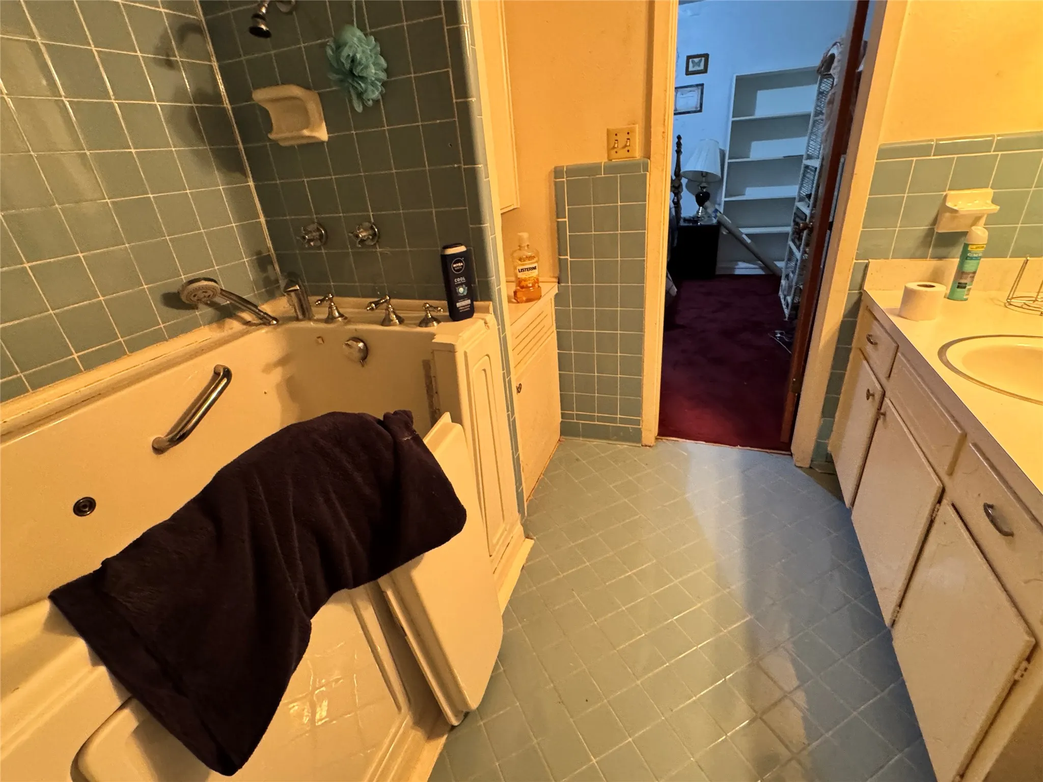 Bathroom featuring light blue tiled flooring and wall accents, a built-in walk-in tub with grab bar, and an overhead shower fixture and a vanity with an sink,