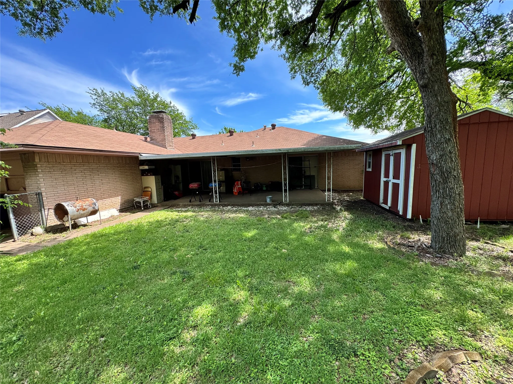 Expansive backyard featuring a lawn, a covered patio with support columns, and a detached storage shed with double doors