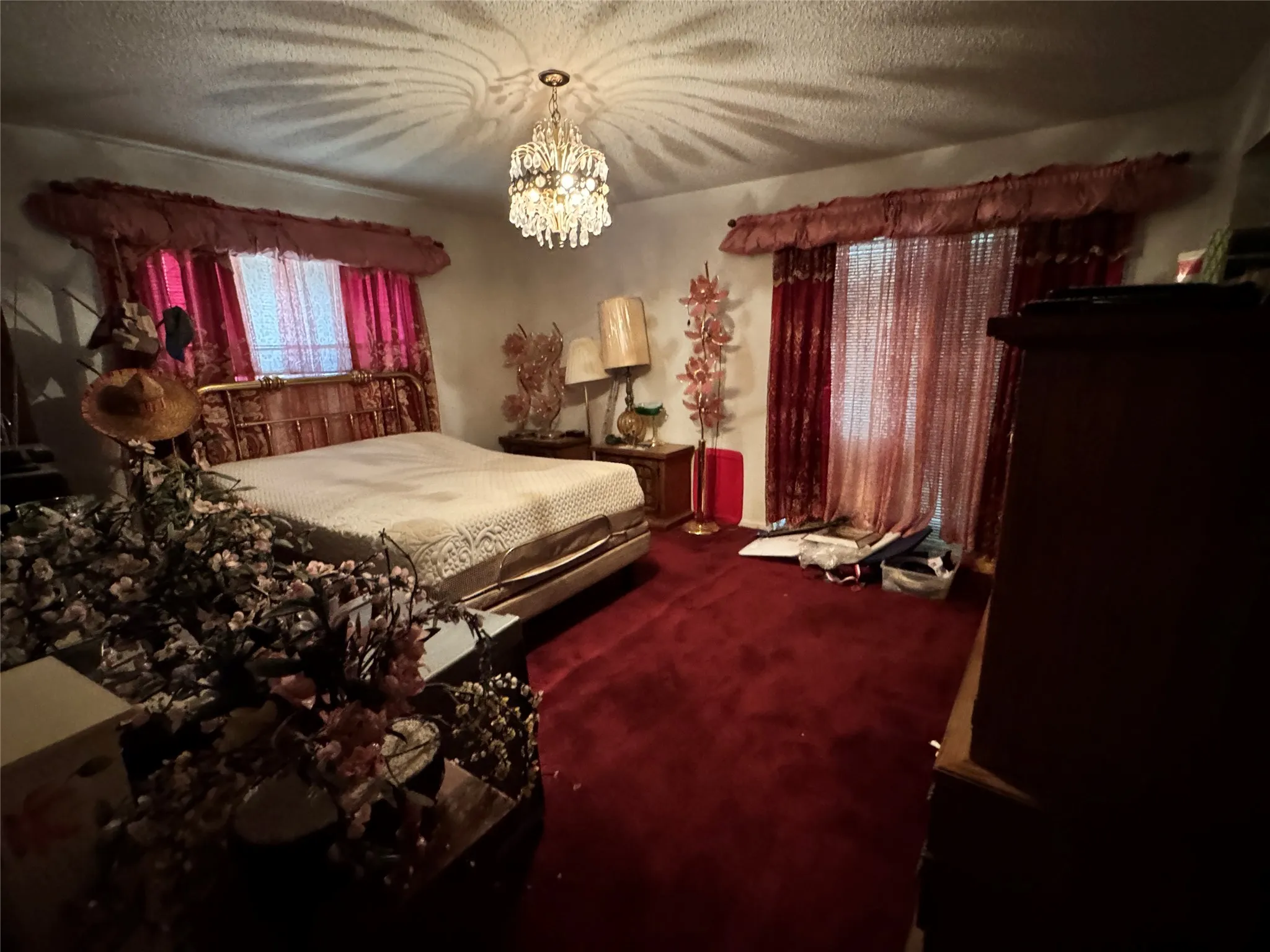 Bedroom featuring a chandelier, red carpeting, a decorative metal bed frame, and window treatments with valances