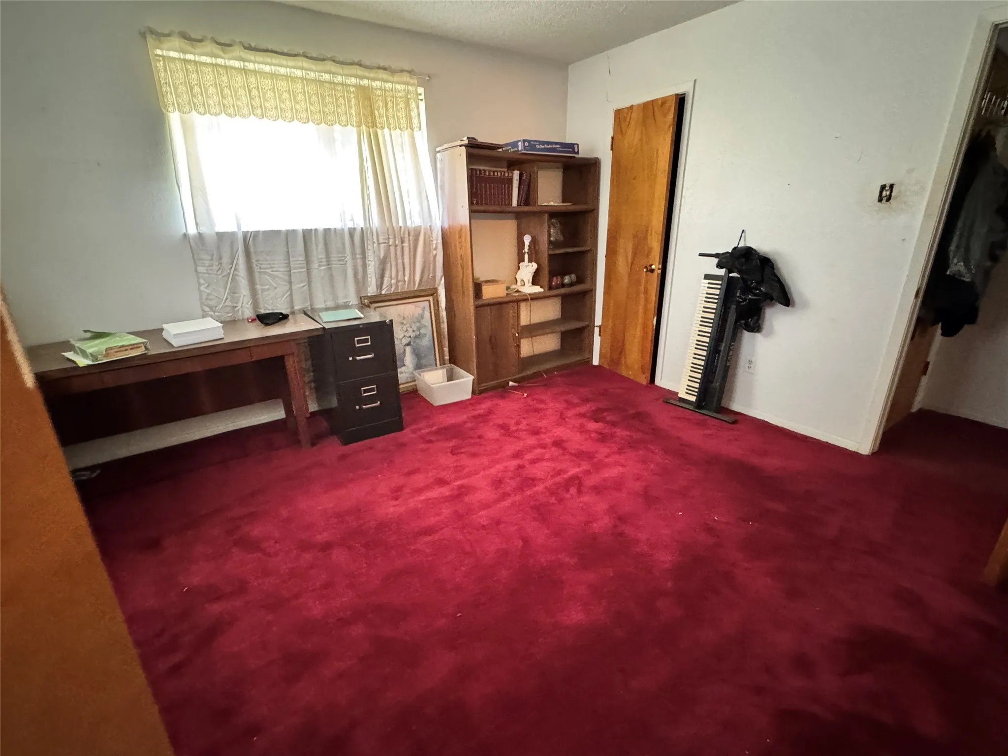 Room featuring red carpeting, a window with curtains, and a built-in wooden shelving unit