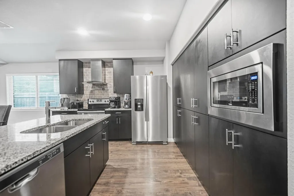 Modern kitchen featuring dark cabinetry, stainless steel appliances, a built-in microwave, and wood-finish flooring