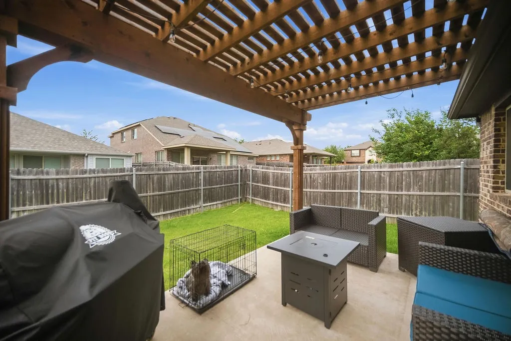Spacious patio featuring a wood pergola with string lighting, concrete flooring, and a privacy fence enclosing a grass yard