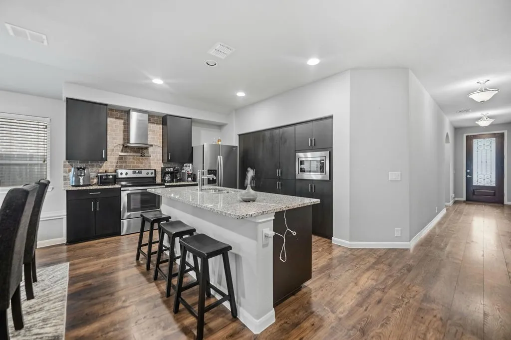 Modern kitchen featuring dark cabinetry, stainless steel appliances, a center island with a light-toned countertop, and wood-finish flooring