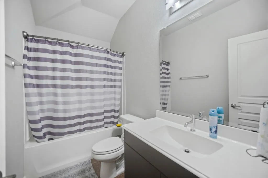 Bathroom featuring a built-in tub with shower, white toilet, and a vanity with an integrated sink