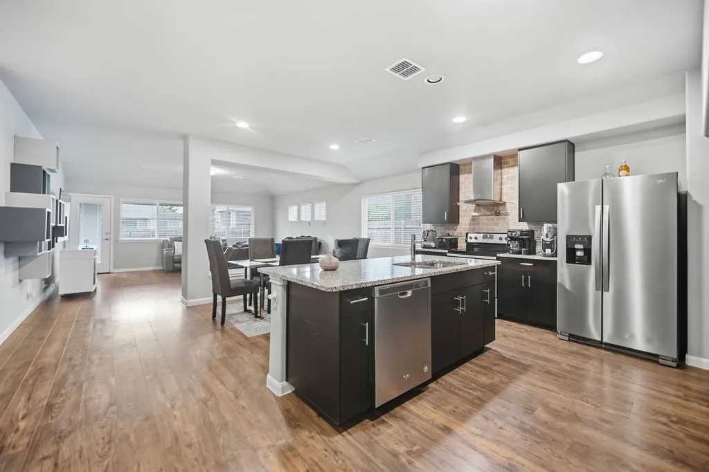 Kitchen featuring wood-finish flooring, dark cabinetry, stainless steel appliances, a center island with a granite-style countertop, and recessed lighting