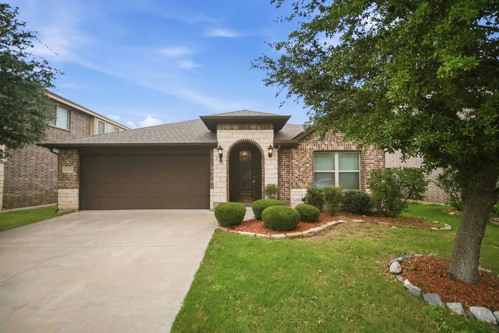 Brick and stone facade residence featuring an arched entry, mature front yard landscaping with a large tree, a paved driveway, and an attached two-car garage