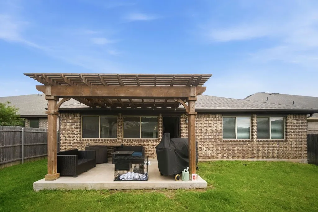 Spacious backyard featuring a wood pergola over a concrete patio, a brick exterior, and a manicured lawn