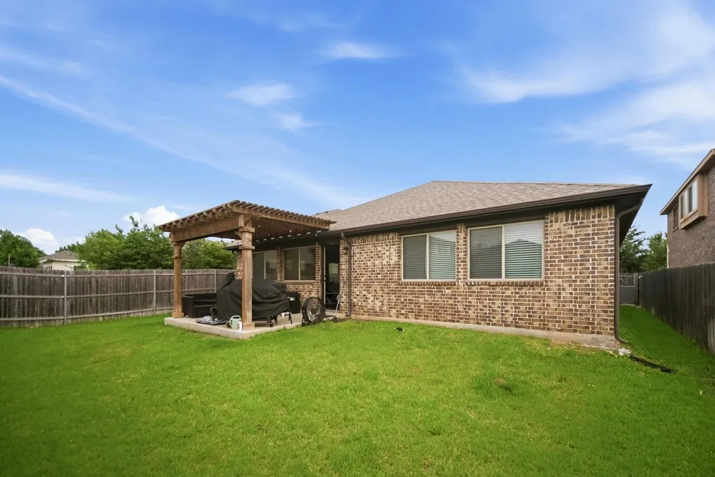 Expansive backyard featuring a pergola-covered patio, brick exterior, multiple windows, and a wood privacy fence