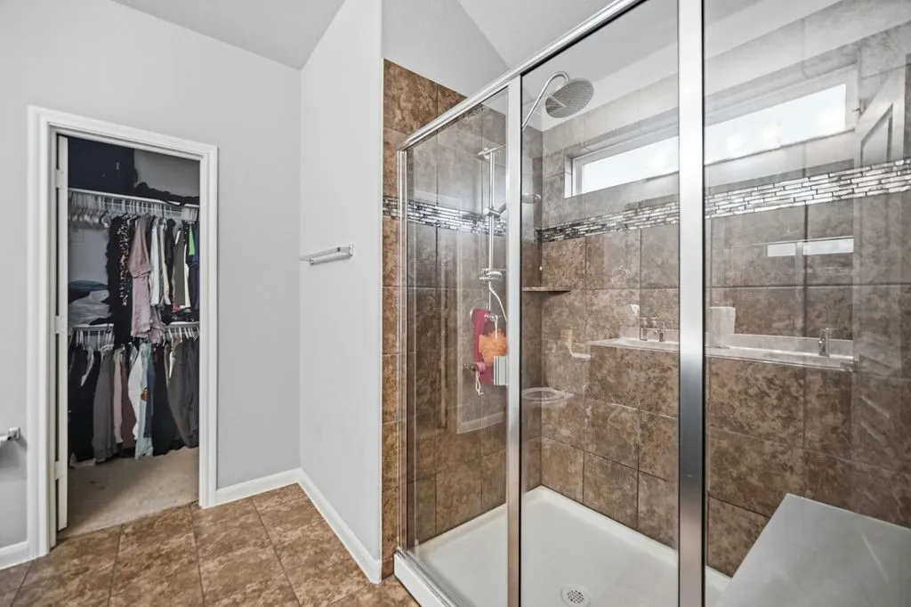 Shower with glass enclosure, brown tile surround, built-in shelving, and a rain shower head