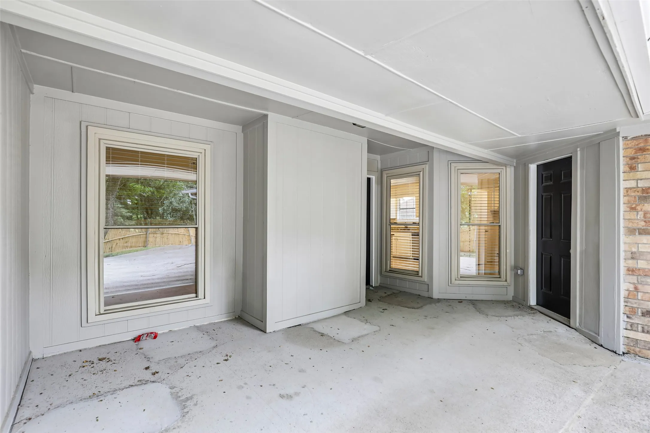 Covered patio with a concrete slab floor, light gray vertical paneling, and multiple windows with blinds