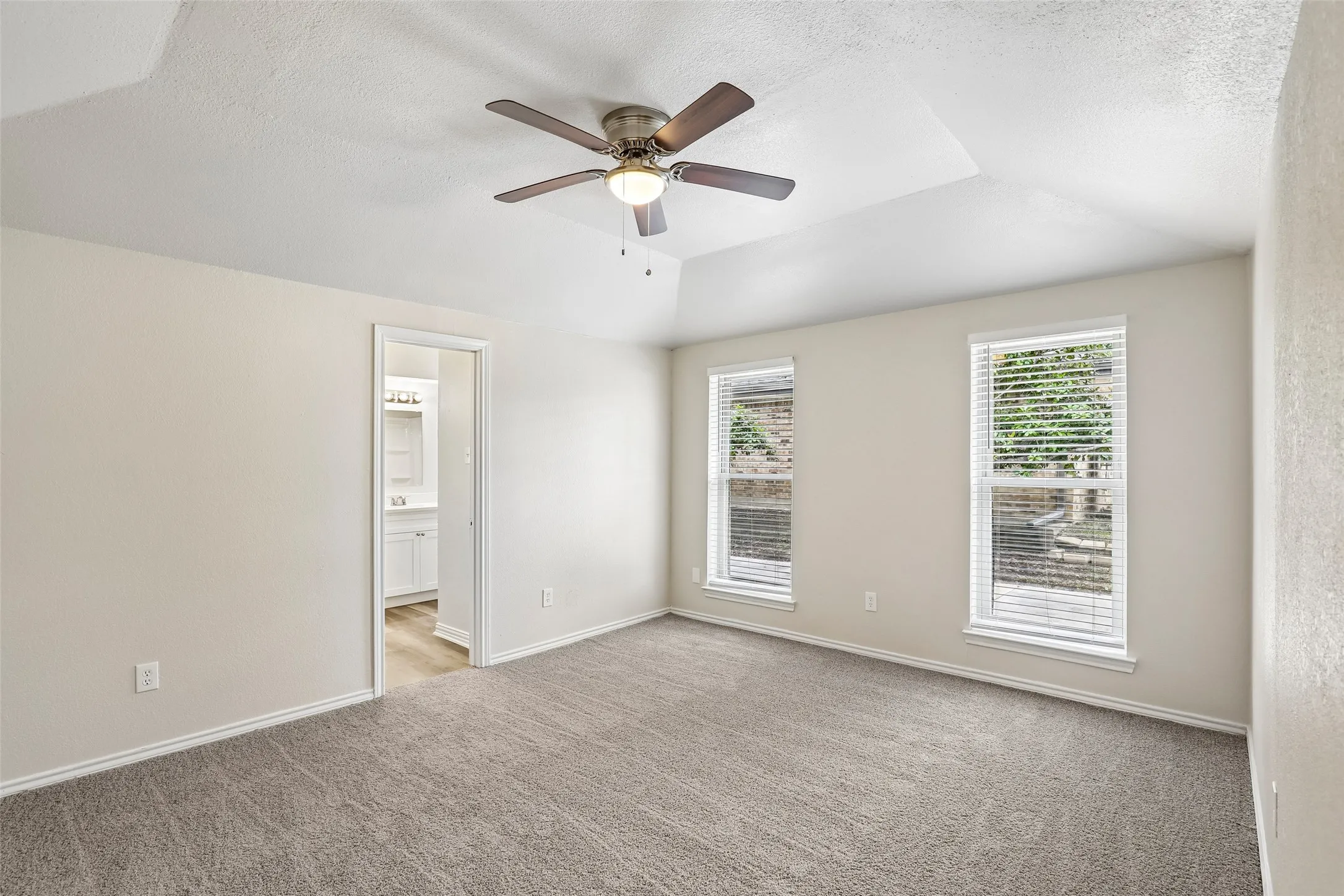 Spacious room featuring a tray ceiling, ceiling fan with integrated lighting, and two windows with blinds
