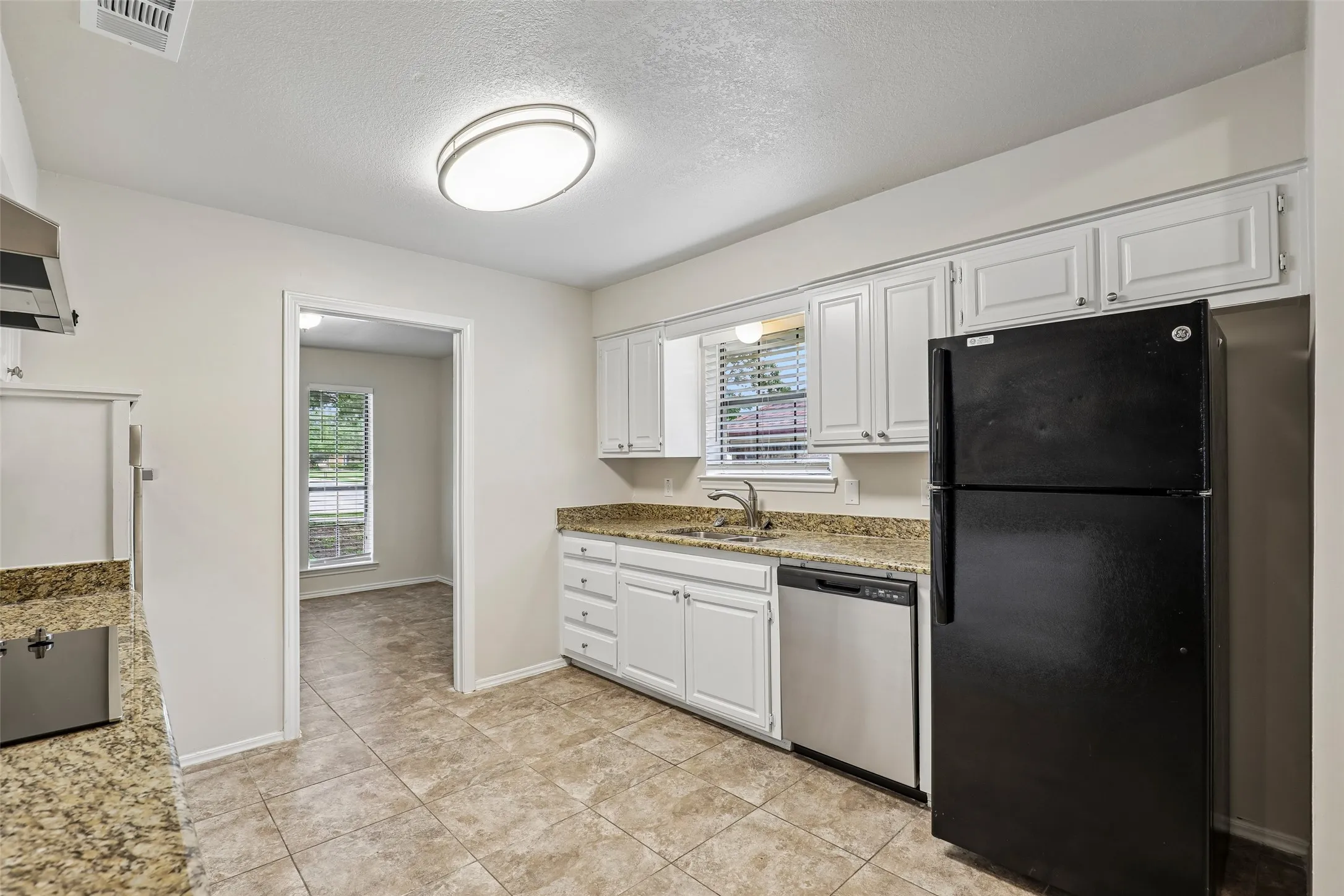 Kitchen featuring white shaker-style cabinetry, granite-finish countertops, tile flooring, and a stainless steel dishwasher