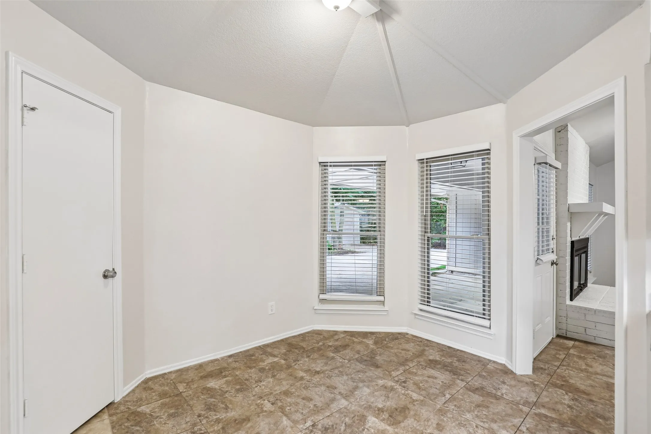 Bay window area featuring two windows with blinds, a vaulted ceiling, and neutral-toned tile flooring