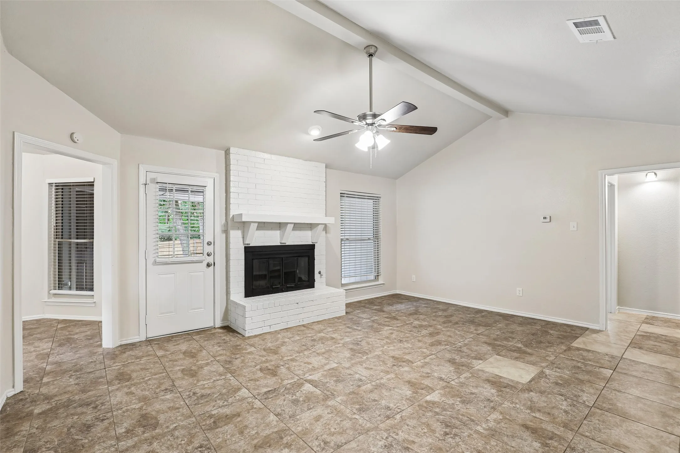Spacious living area featuring a vaulted ceiling with exposed beams, an overhead ceiling fan, and tile flooring