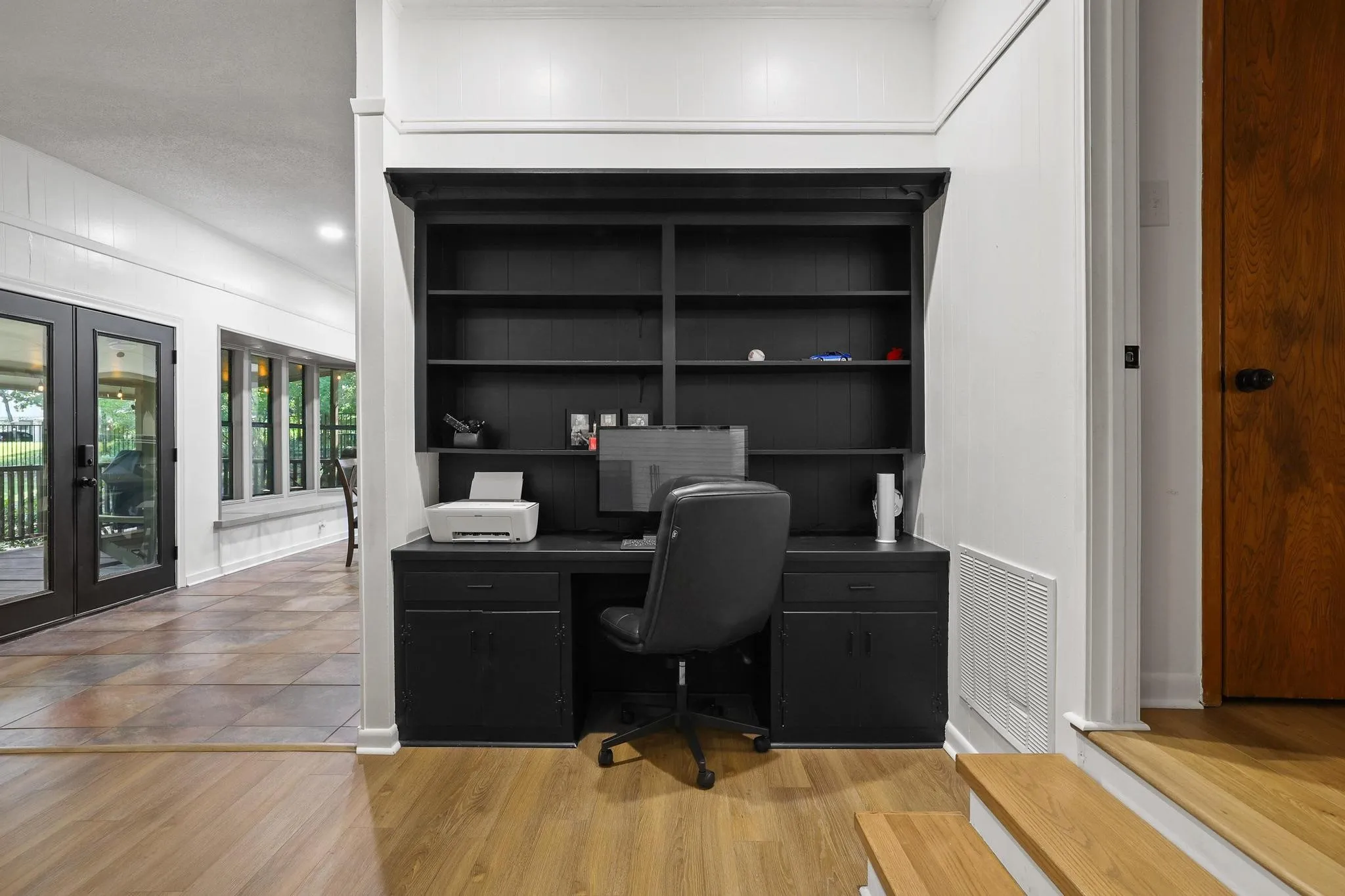 Built-in desk area featuring a dark finish, integrated shelving, lower cabinetry, and wood-finish flooring