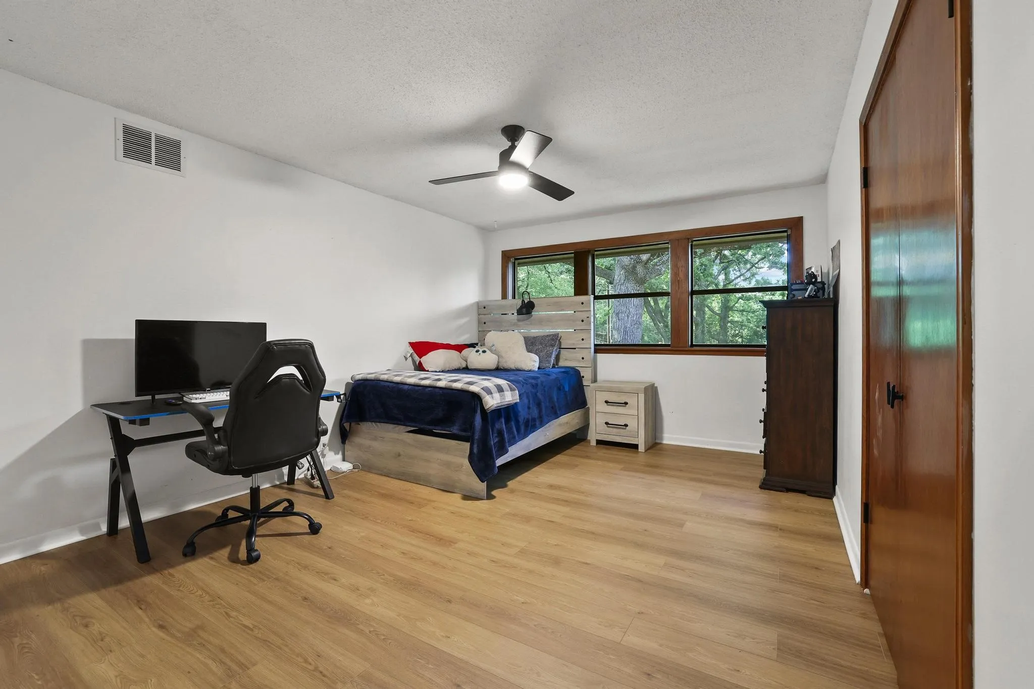 Spacious bedroom featuring wood-finish flooring and a ceiling fan with integrated lighting
