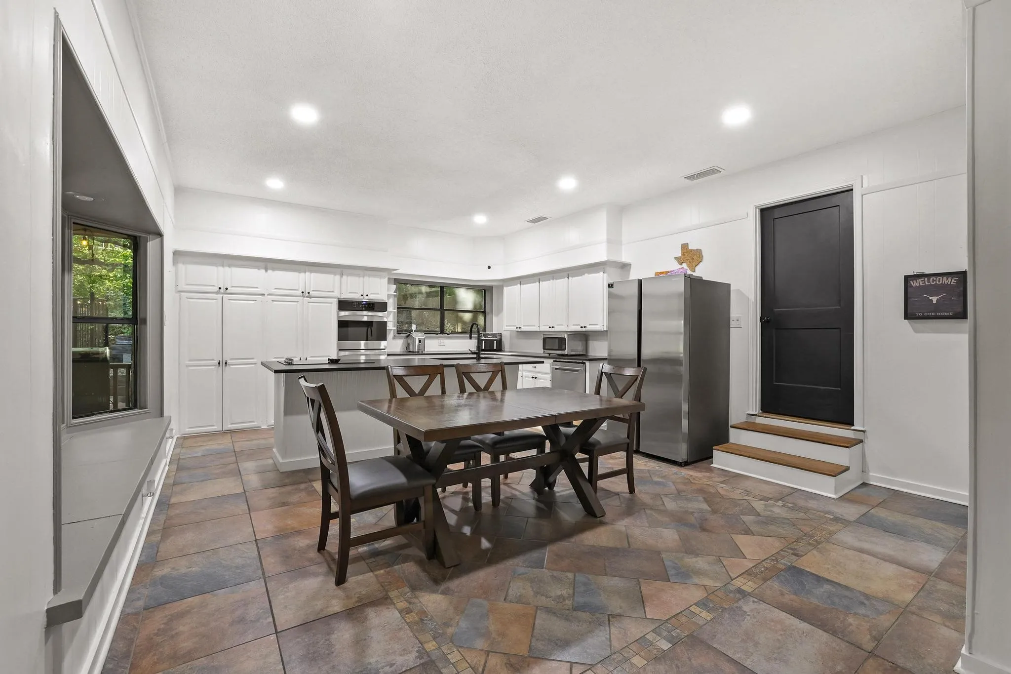 Spacious kitchen featuring extensive white cabinetry, stainless steel appliances, and a central island with black countertops