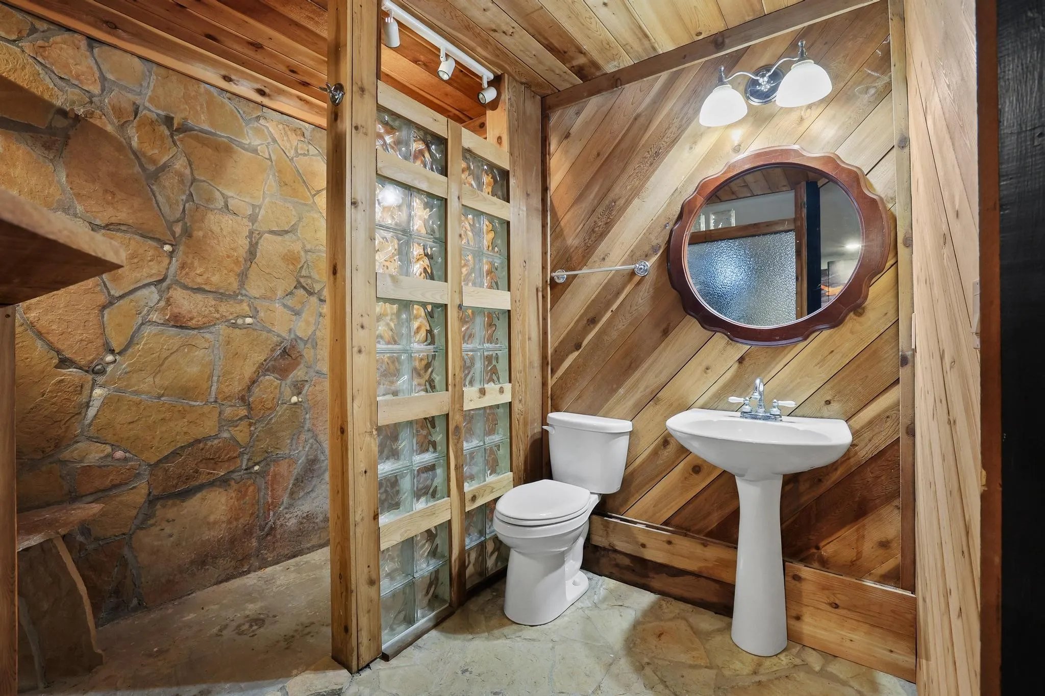 Bathroom featuring wood-paneled walls, stone-tiled shower, and a glass block shower enclosure