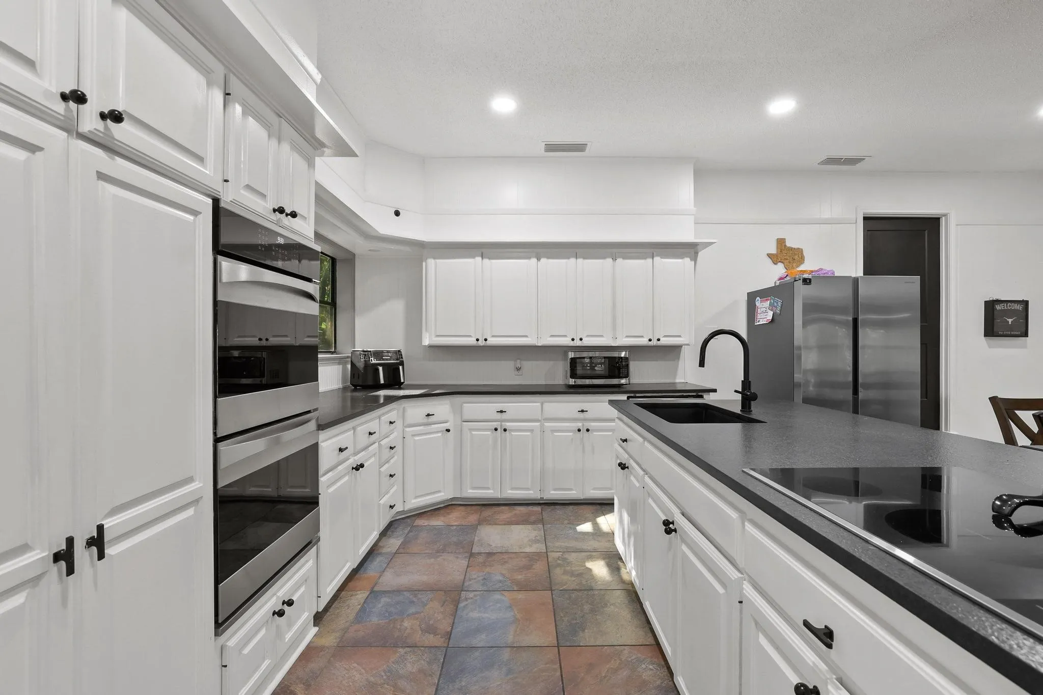 Modern kitchen featuring white cabinetry with black hardware, dark countertops, and stainless steel built-in ovens
