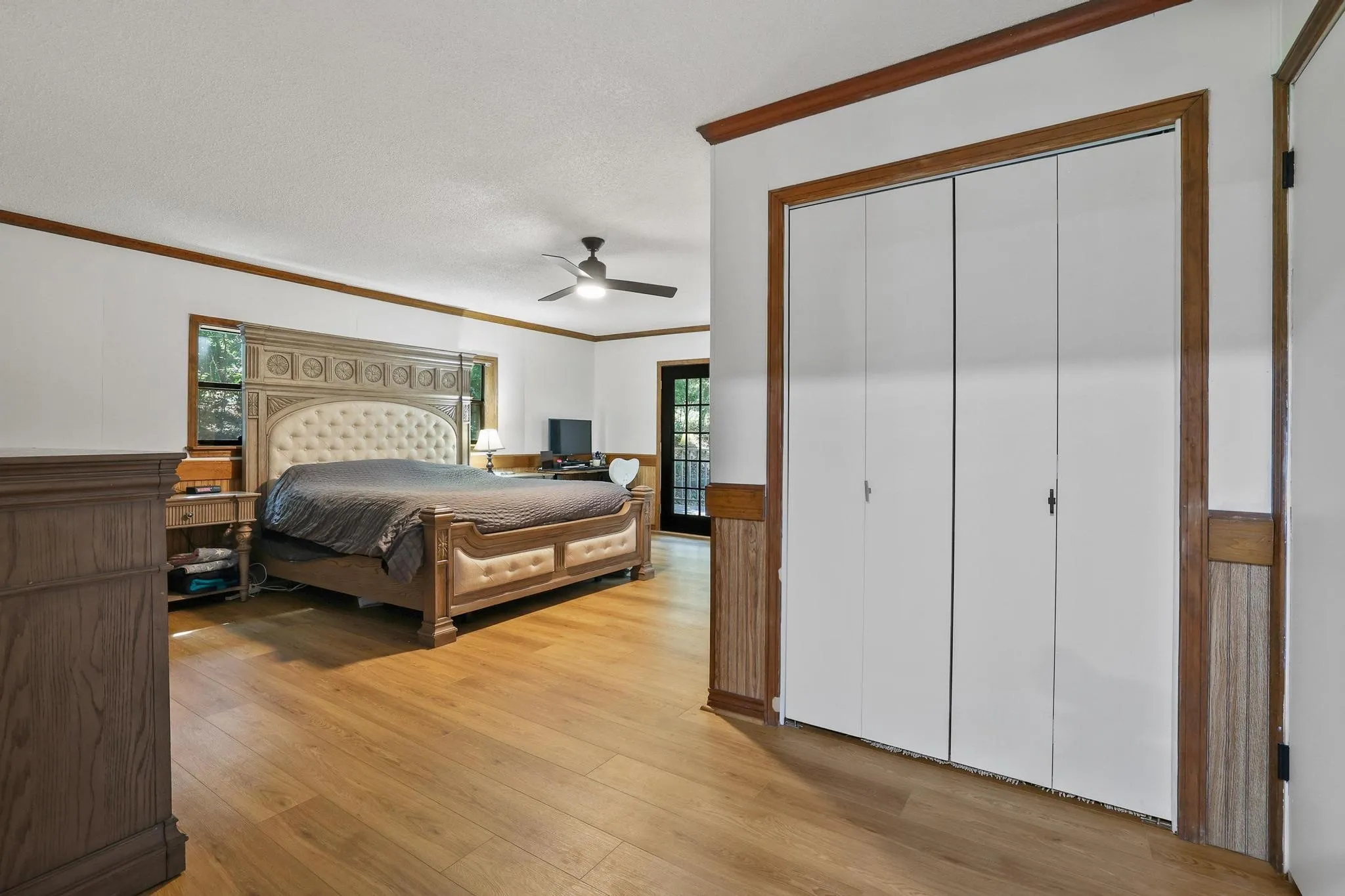 Spacious room featuring wood-finish flooring, white walls with wood trim, a ceiling fan, and a built-in closet with bi-fold doors