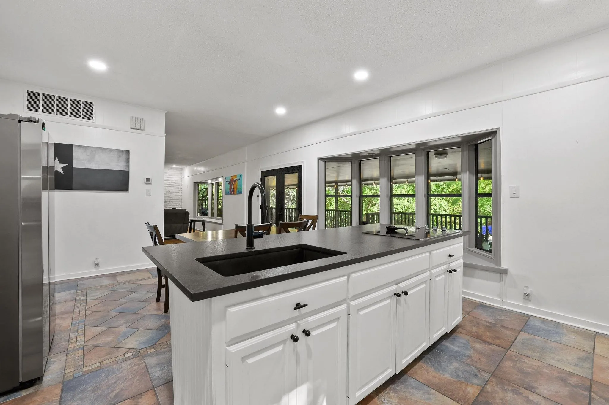 Kitchen island with an undermount sink and matte black faucet, dark countertops, and white cabinetry