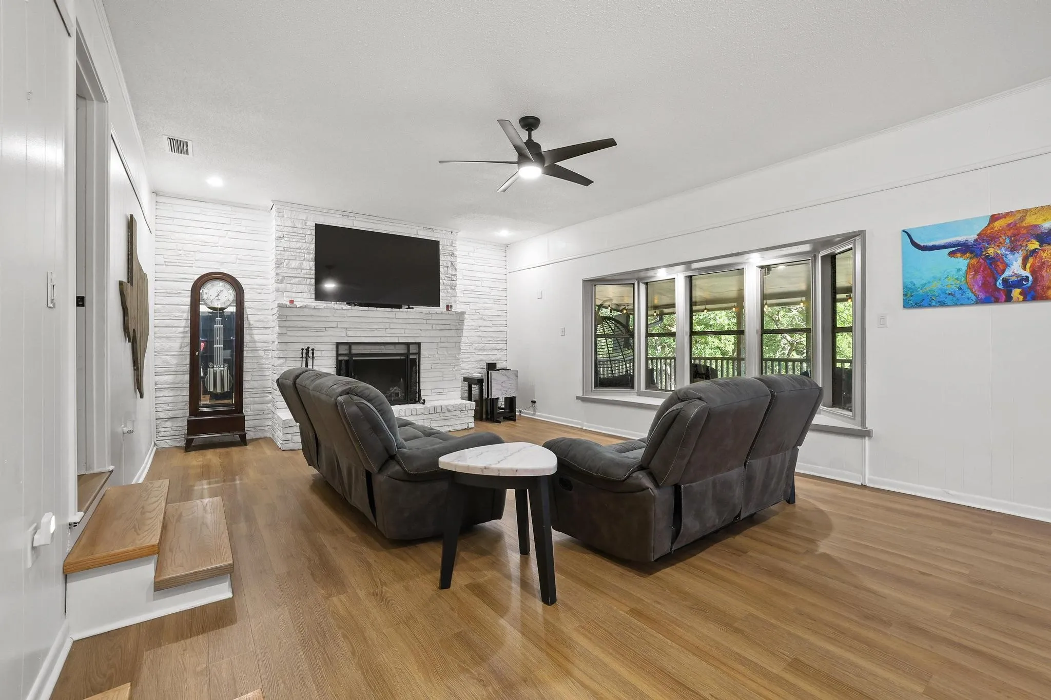 Spacious living area featuring wood-finish flooring, a white brick fireplace, and a bay window