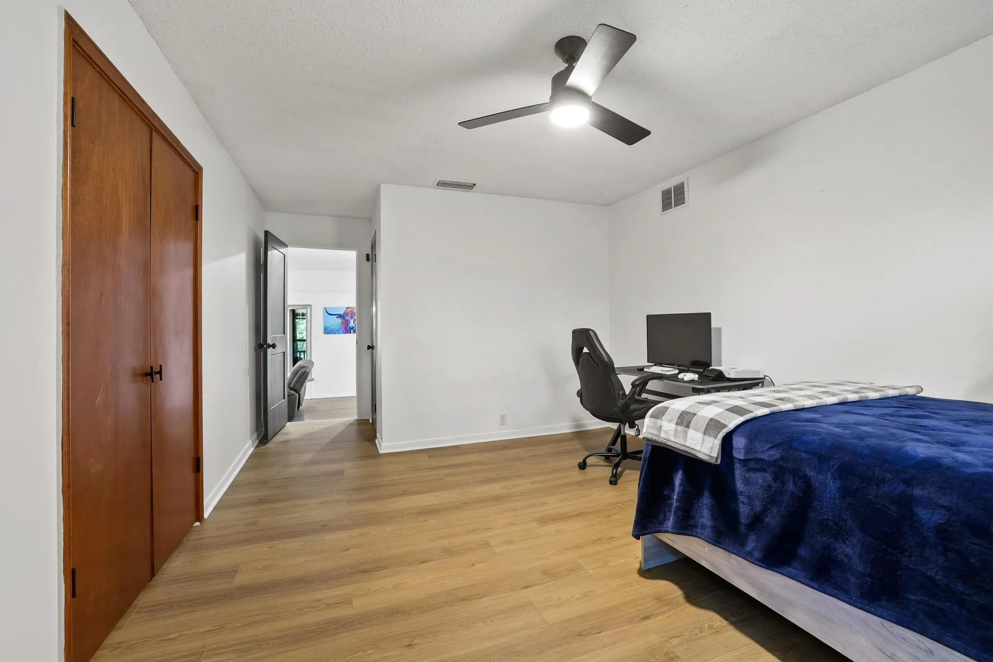 Interior room featuring wood-finish flooring, white painted walls, and a ceiling fan with integrated lighting