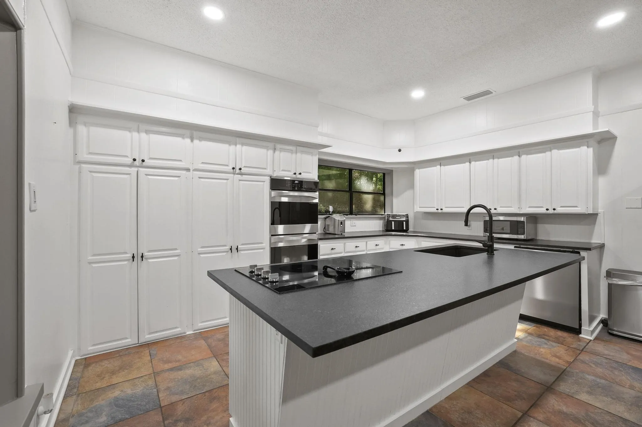 Kitchen featuring a large center island with built-in cooktop, ample white cabinetry, stainless steel double wall ovens, and multi-toned tile flooring