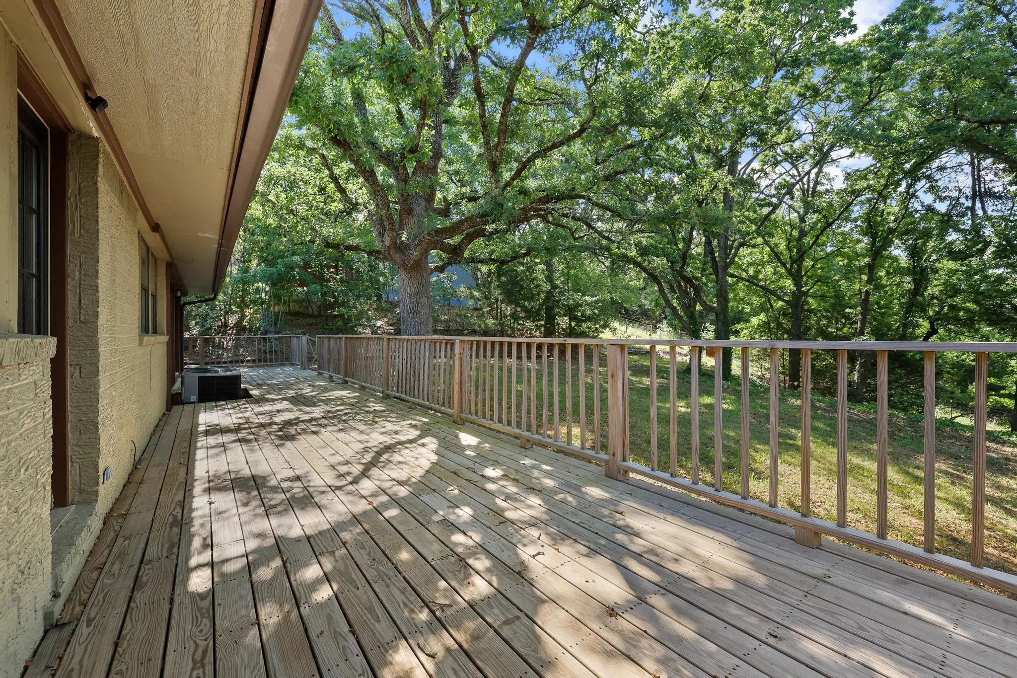 Expansive wood deck with natural wood railing overlooking a sloped, treed landscape