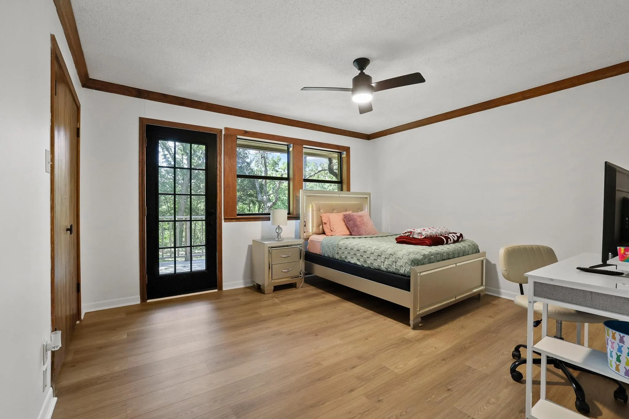 Spacious room featuring wood-finish flooring, a ceiling fan with integrated lighting, and white walls complemented by dark wood trim