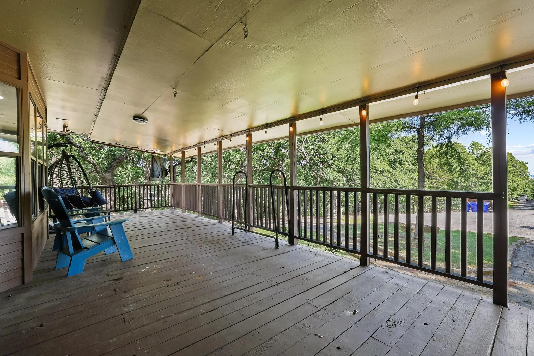 Expansive covered porch featuring wood-finish flooring, a full-length railing, and string lighting