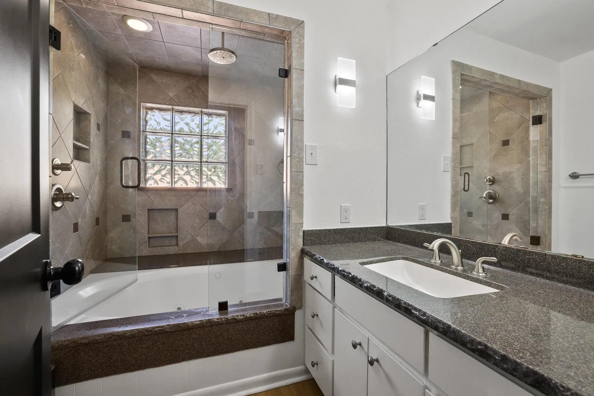 Bathroom featuring a tiled shower and soaking tub combination with a glass enclosure, a rain showerhead, a built-in shower niche, and a glass block window