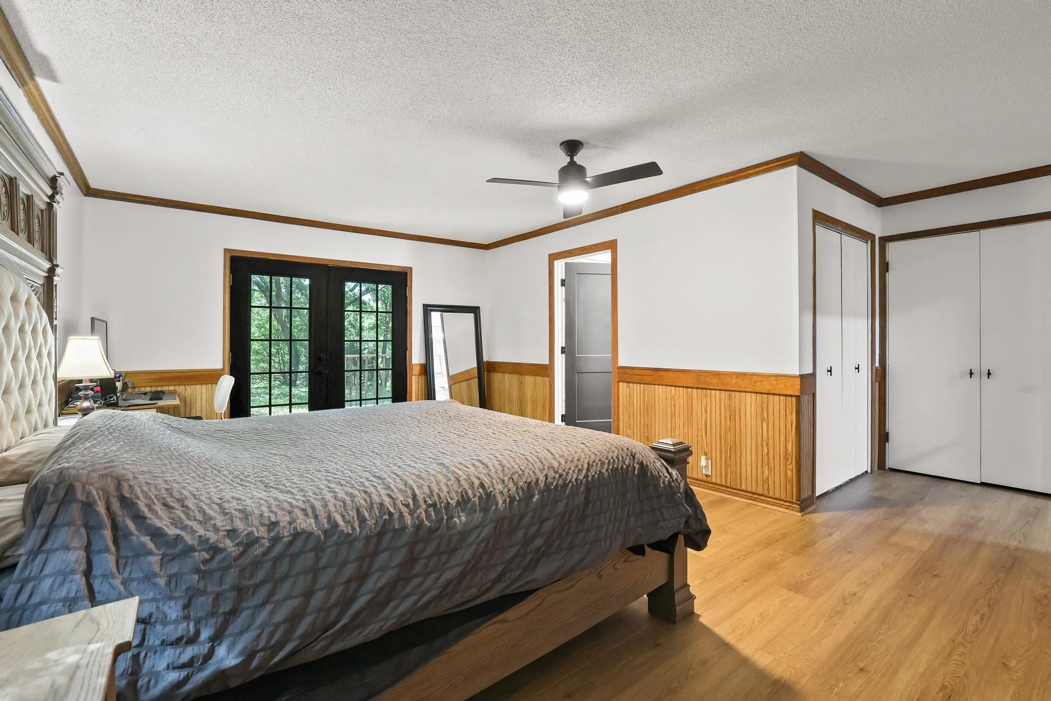 Room featuring light wood-finish flooring, white walls with wood paneling, and a black ceiling fan