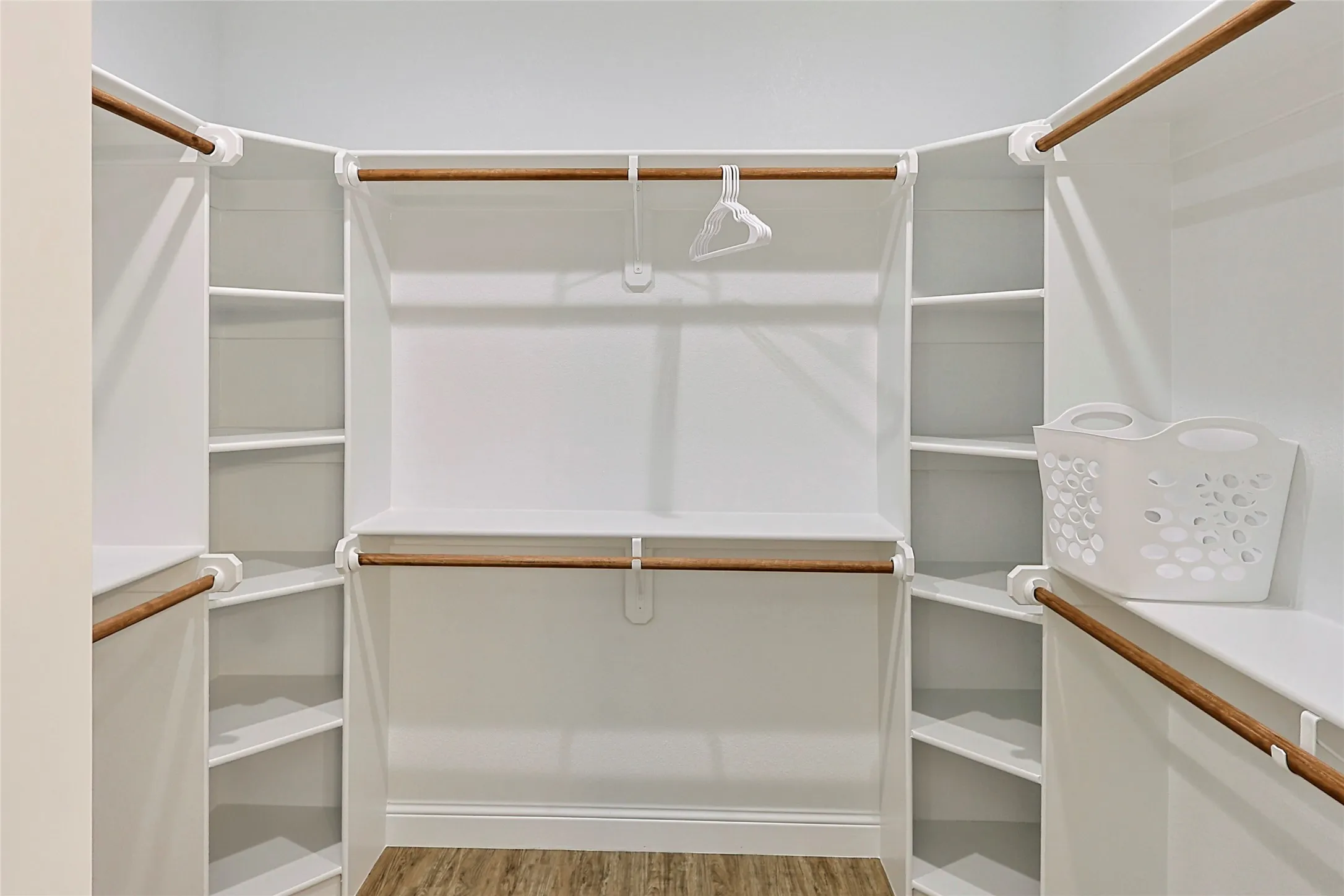 Custom closet system featuring wood-finish flooring, white shelving, and multiple hanging rods