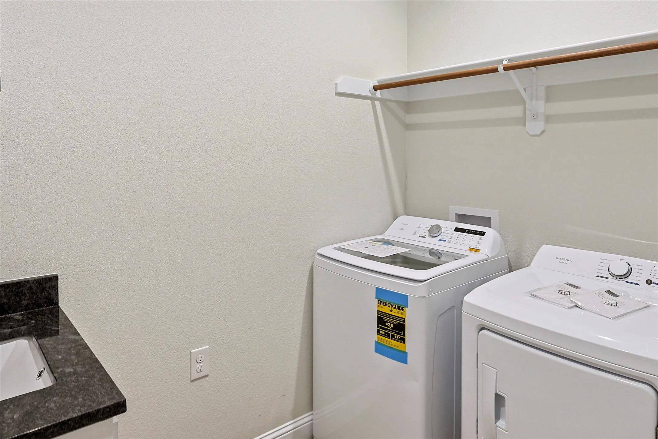 Dedicated laundry area featuring a built-in hanging rod, textured walls, and a dark stone-finish countertop with an undermount sink