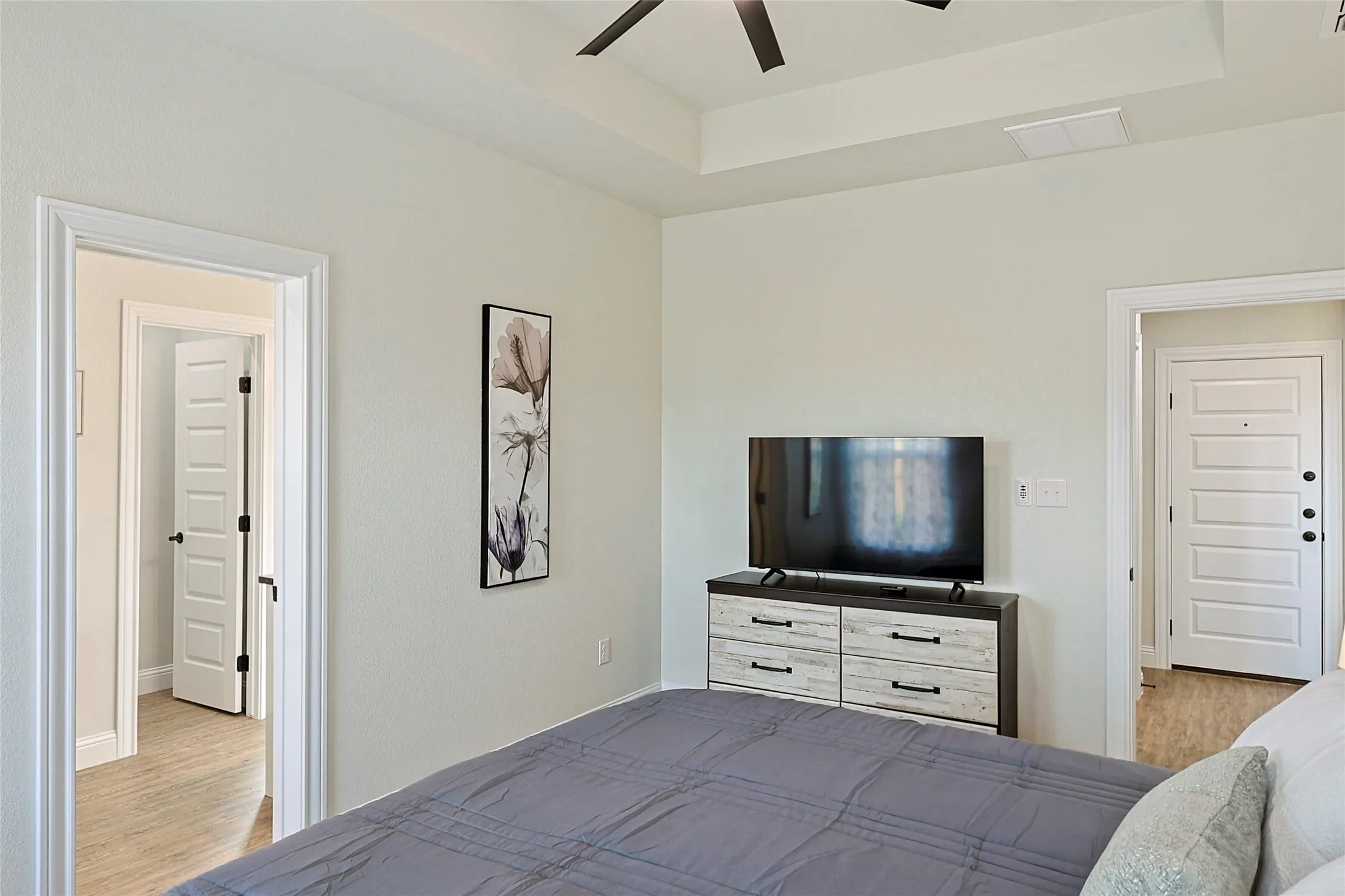 Tray ceiling with a ceiling fan, light neutral wall paint, and wood-finish flooring