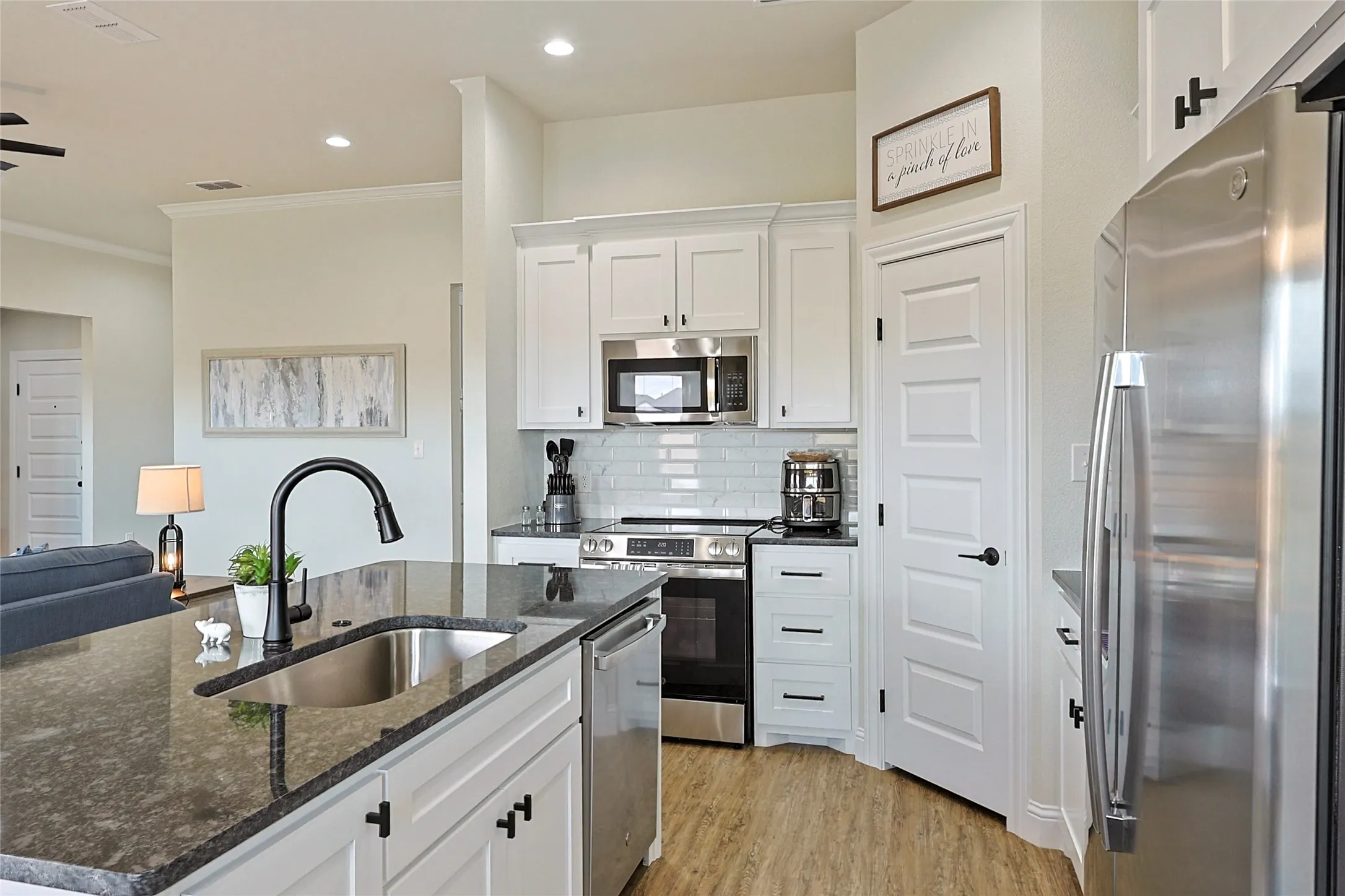 Kitchen featuring a dark stone island with an undermount sink and matte black faucet, stainless steel appliances, white cabinetry, and a white subway tile backsplash
