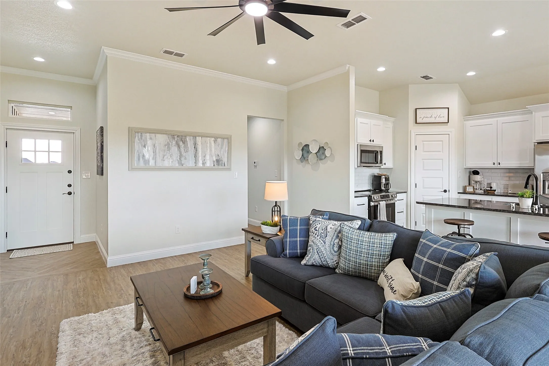 Open-concept living area featuring a kitchen with white cabinetry and dark countertops, wood-finish flooring, recessed lighting, and a ceiling fan