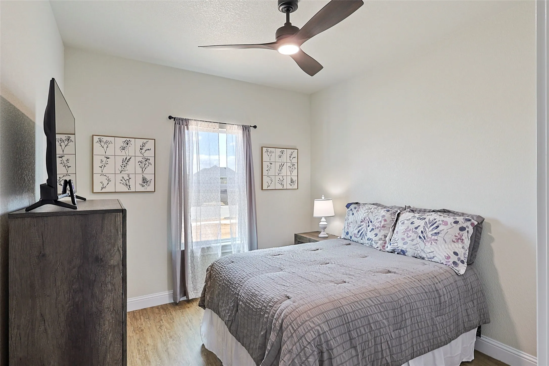 Bedroom featuring wood-finish flooring, a contemporary ceiling fan with integrated lighting, a window with sheer and solid drapes, and neutral wall tones