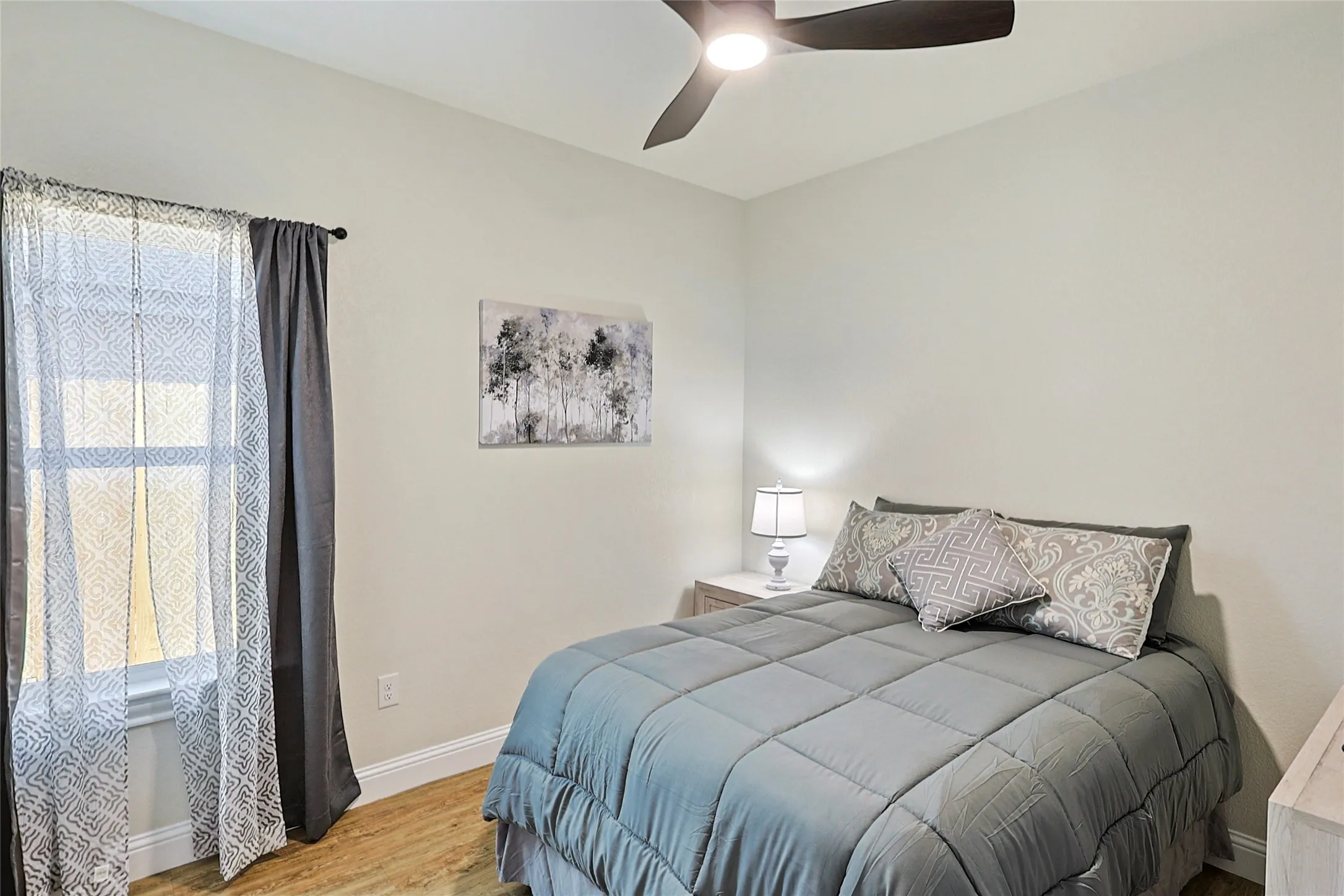 Bedroom featuring wood-finish flooring, a contemporary ceiling fan with integrated lighting, and a window with white trim