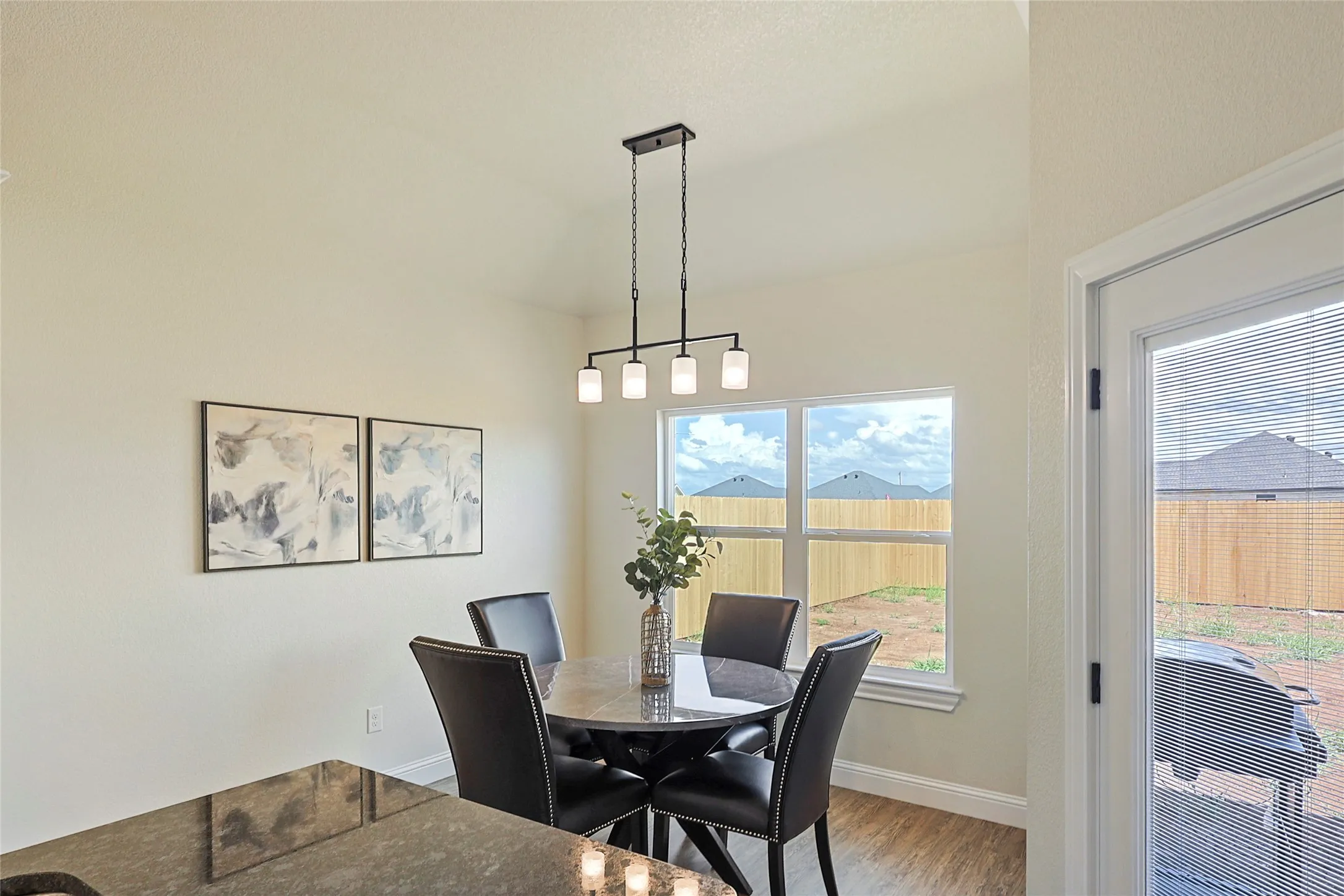 Dining area featuring a modern linear chandelier, a large window with backyard views, and wood-finish flooring
