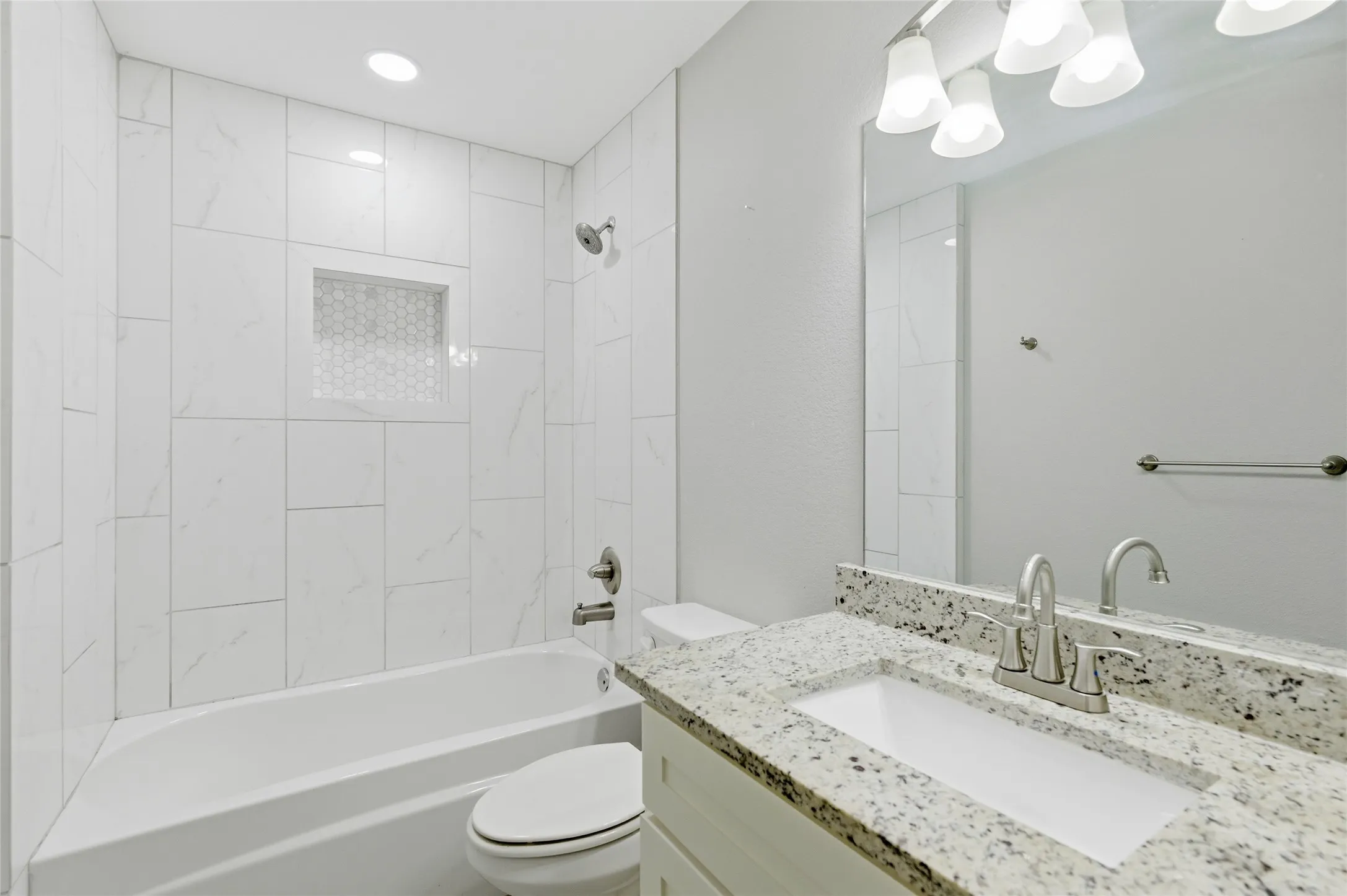 Bathroom with a tub/shower combination, white subway tile surround, recessed niche with mosaic tile accent, and a vanity featuring a white granite countertop and integrated sink