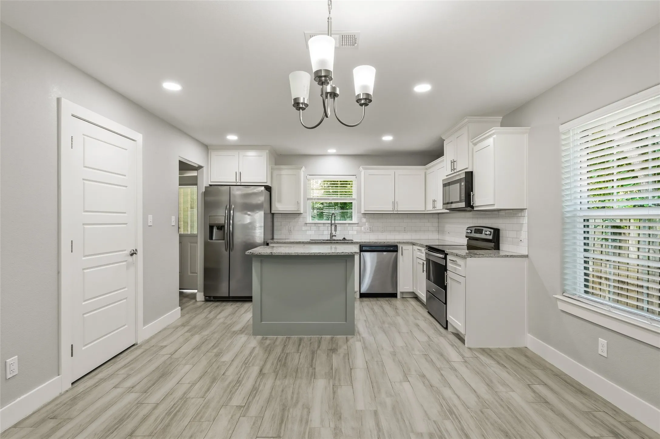 Open-concept kitchen featuring an island with a contrasting base, stainless steel appliances, white cabinetry, and ceramic tile flooring