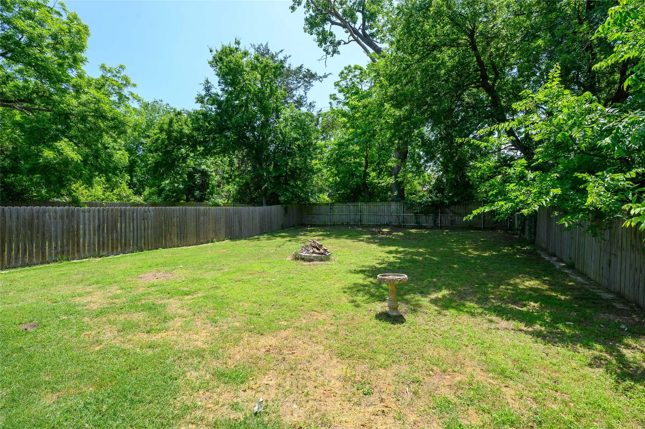 Expansive private backyard with a wood privacy fence, mature trees, and a fire pit