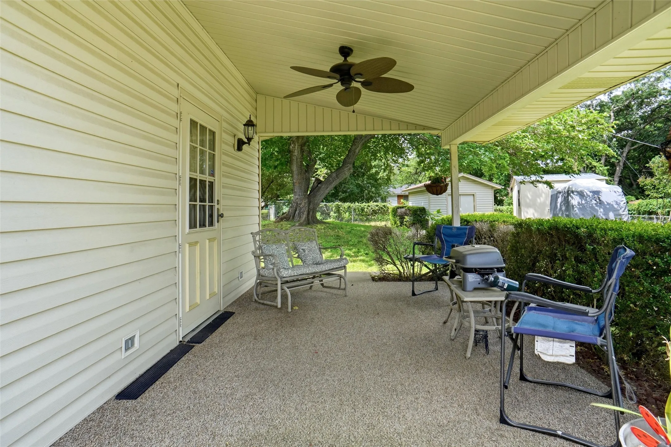 Covered outdoor patio with a textured concrete surface, featuring a ceiling fan and exterior lighting fixtures